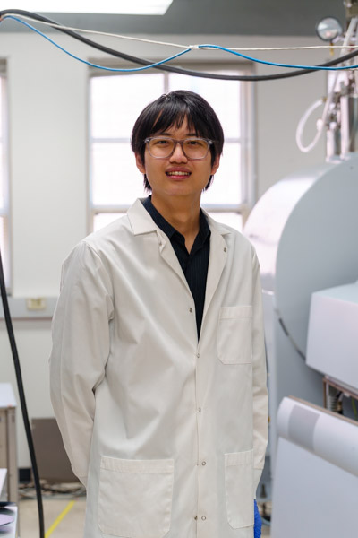 Yu Tin Lin, Knight Hennessy Scholar, standing in a white laboratory, posing with his arms behind his back and smiling in a white lab coat.
