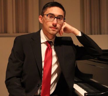 Professional headshot of Ben Vantoorenburg, President and Chair of SACUA at UF. He is wearing a suit with a red tie, leaning on a grand piano.