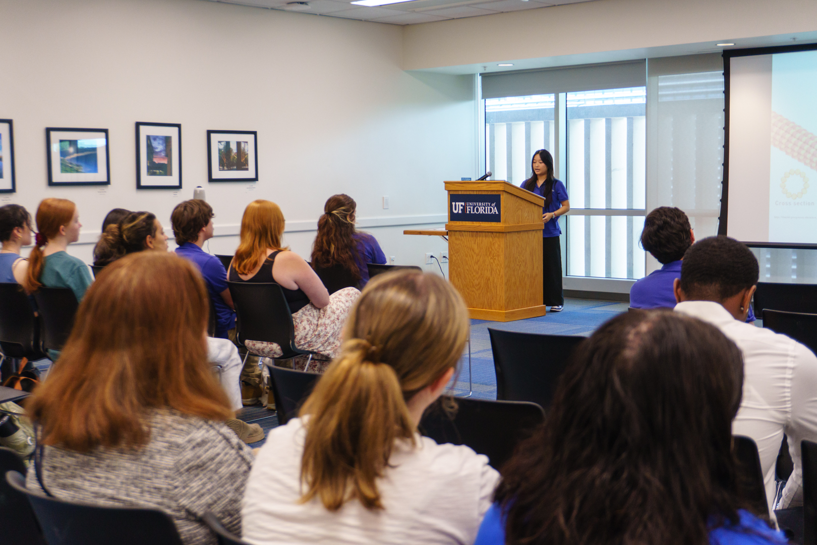 A seated crowd watches a McNair Scholar present from behind a wooden podium.