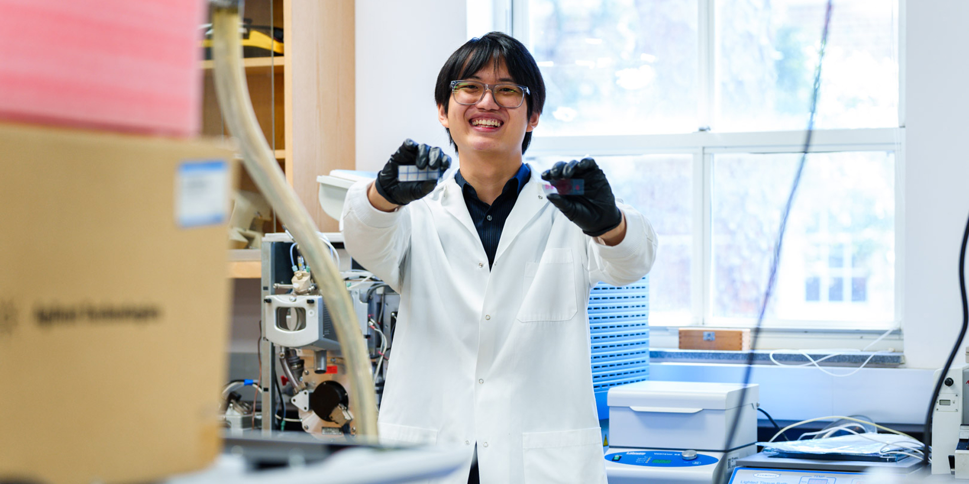 Yu Tin holding up two glass microscope slides in the Prentice Lab.