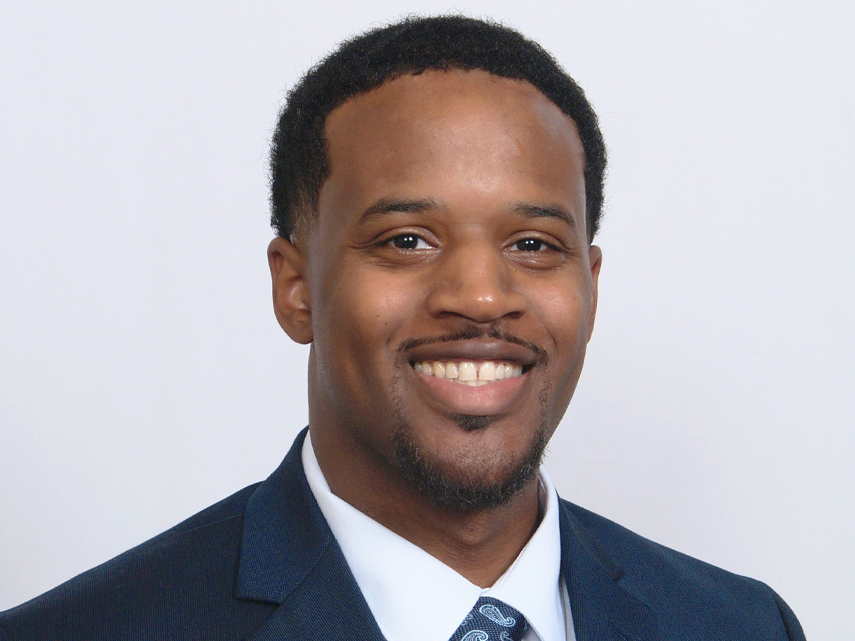 Nigel Richardson smiles in a blue suit in front of a white background.