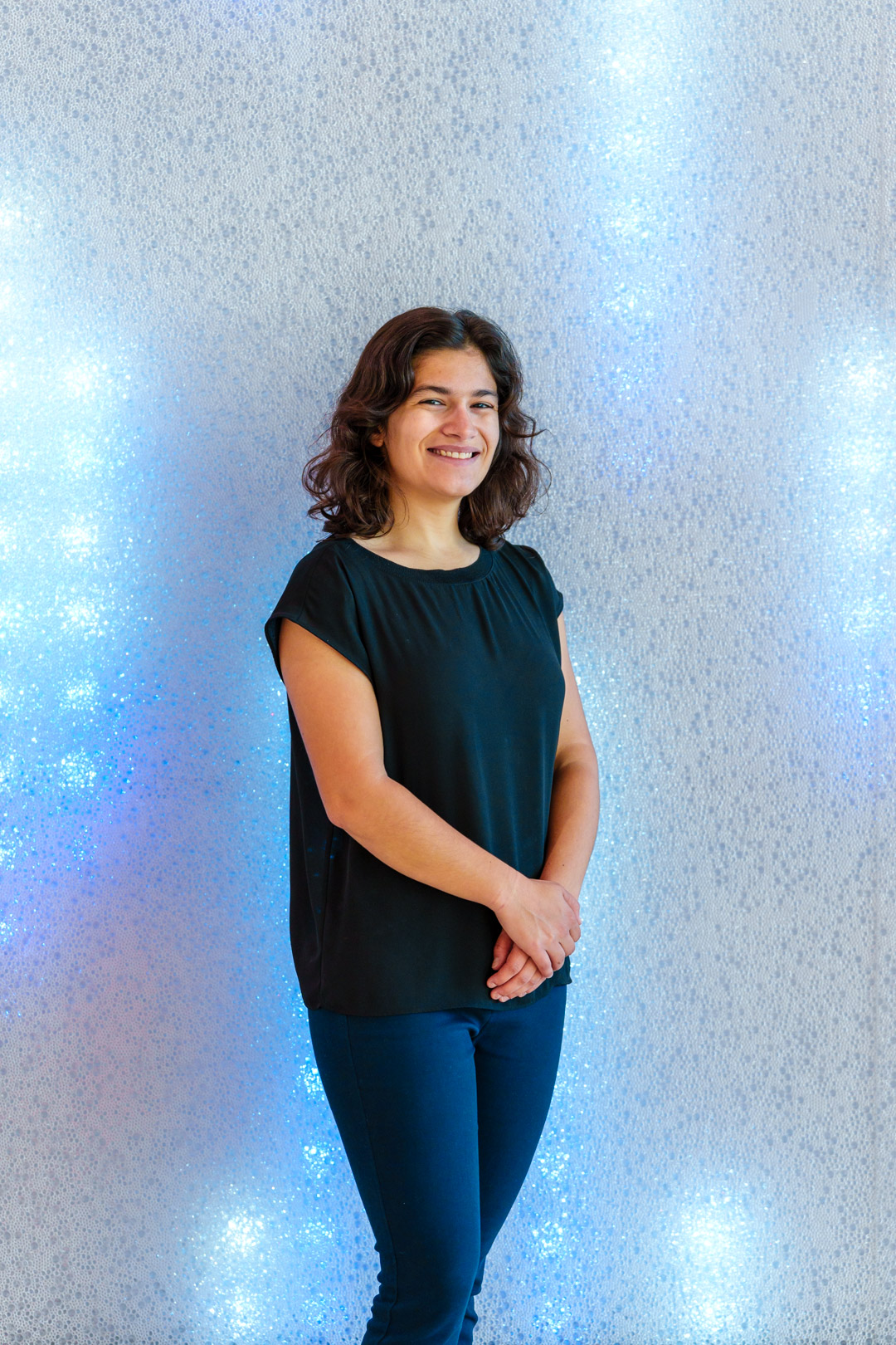 A portrait of Sofia Aviles posing in front of a sparkling wall of LED lights.