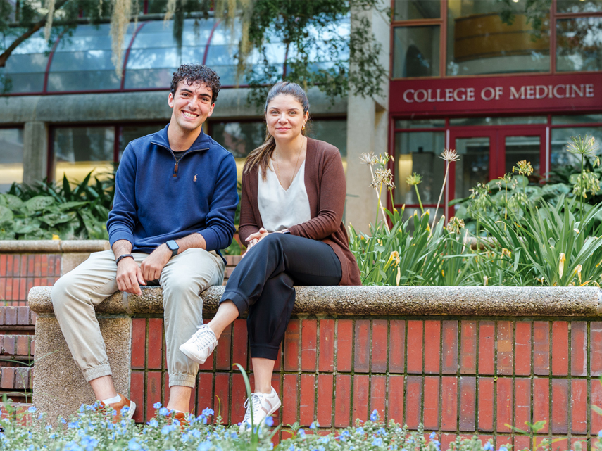 Sultan Khanfar and Dr. Aline Oliveira sit on a ledge in front of the College of Medicine.