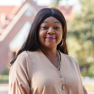 Angeleah Browdy in a tan dress shirt. A brick building and tree are behind her.