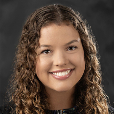 Hanna Clark smiles for a professional headshot in front of a grey background.